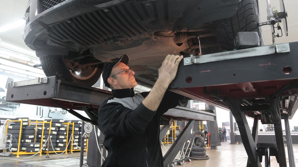 Mechanic inspecting car on lift in an automotive garage, focusing on vehicle repair and maintenance.